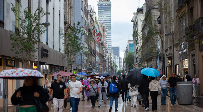 people walk through mexico city with umbrellas, with the latin america tower in the backgound