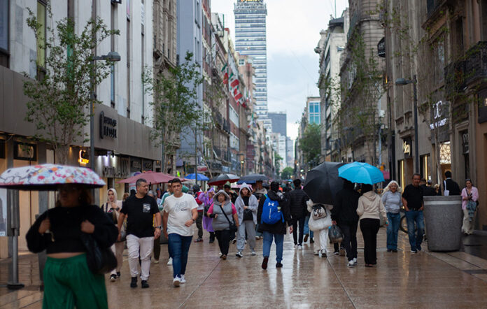 people walk through mexico city with umbrellas, with the latin america tower in the backgound