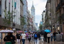 people walk through mexico city with umbrellas, with the latin america tower in the backgound