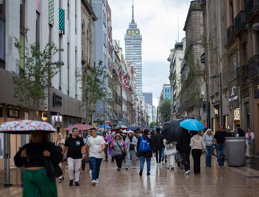 people walk through mexico city with umbrellas, with the latin america tower in the backgound