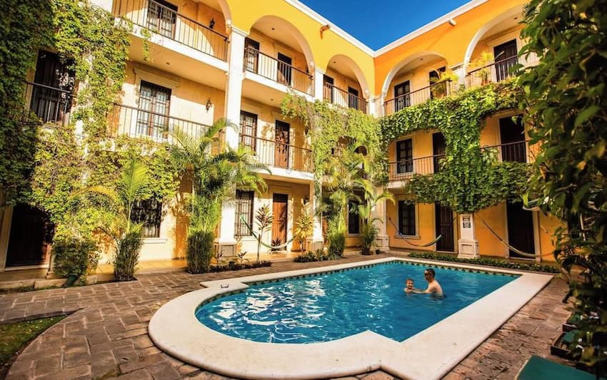 A colonial hotel with yellow walls and white arches. A swimming pool is in the foreground.