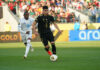 A soccer player in the black Mexican uniform dribbles ahead of another player in a white and blue uniform