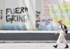 A blonde woman walks past graffiti reading "Fuera gringo" in Mexico City