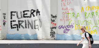 A blonde woman walks past graffiti reading "Fuera gringo" in Mexico City