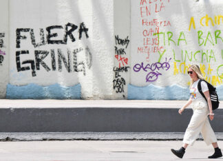 A blonde woman walks past graffiti reading "Fuera gringo" in Mexico City