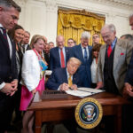 Trump signs a bill surrounded by supporters