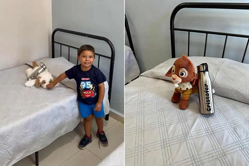 A child stands next to a bed with a water bottle and toy