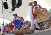 Dancers in traditional garb including long colorful skirts dance on a stage a Guelaguetza in Oaxaca