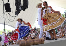 Dancers in traditional garb including long colorful skirts dance on a stage a Guelaguetza in Oaxaca