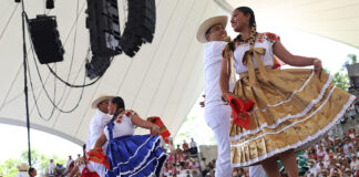 Dancers in traditional garb including long colorful skirts dance on a stage a Guelaguetza in Oaxaca