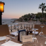 A reserved table at an outdoor restaurant overlooks a beach and ocean at sunset in Los Cabos, Baja California Sur, Mexico