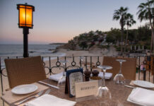 A reserved table at an outdoor restaurant overlooks a beach and ocean at sunset in Los Cabos, Baja California Sur, Mexico