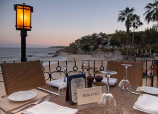 A reserved table at an outdoor restaurant overlooks a beach and ocean at sunset in Los Cabos, Baja California Sur, Mexico