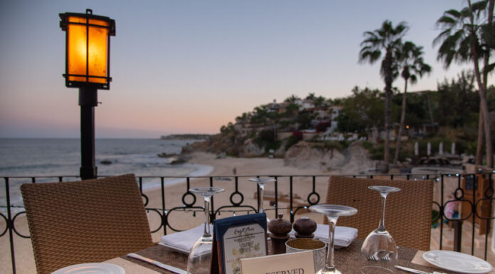 A reserved table at an outdoor restaurant overlooks a beach and ocean at sunset in Los Cabos, Baja California Sur, Mexico