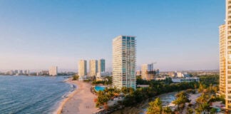 Aerial view of modern high-rise resorts and condominiums lining the sandy beach and coastline of Puerto Vallarta, Mexico, with Banderas Bay stretching into the distance.
