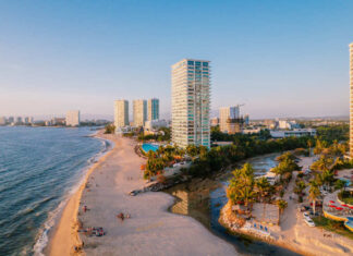 Aerial view of modern high-rise resorts and condominiums lining the sandy beach and coastline of Puerto Vallarta, Mexico, with Banderas Bay stretching into the distance.