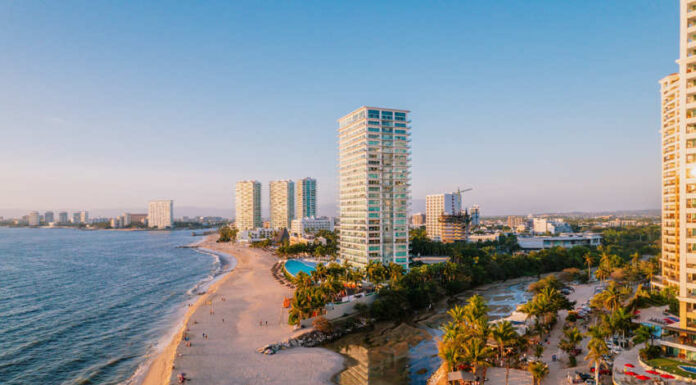 Aerial view of modern high-rise resorts and condominiums lining the sandy beach and coastline of Puerto Vallarta, Mexico, with Banderas Bay stretching into the distance.