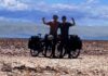 Two cyclists with their arms raised in the air posing in the desert