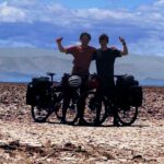 Two cyclists with their arms raised in the air posing in the desert