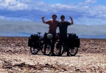 Two cyclists with their arms raised in the air posing in the desert