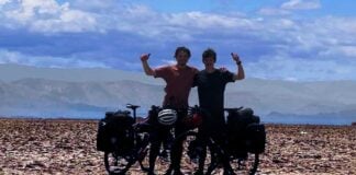 Two cyclists with their arms raised in the air posing in the desert
