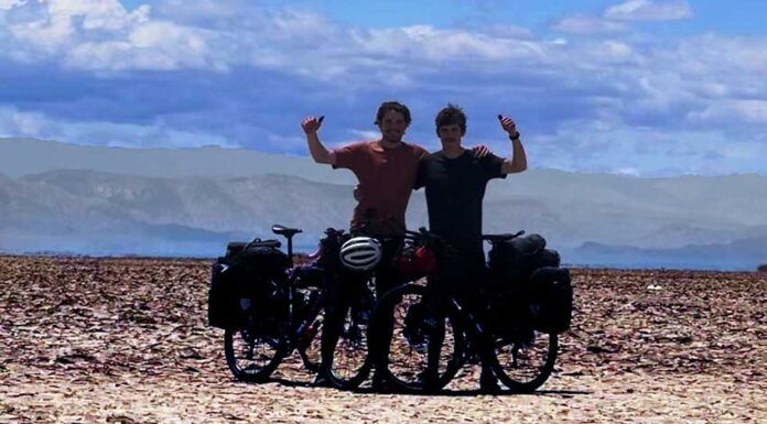 Two cyclists with their arms raised in the air posing in the desert