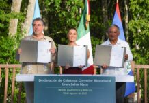 Three heads of state at a podium holding papers