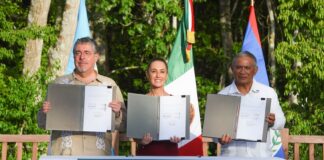 Three heads of state at a podium holding papers