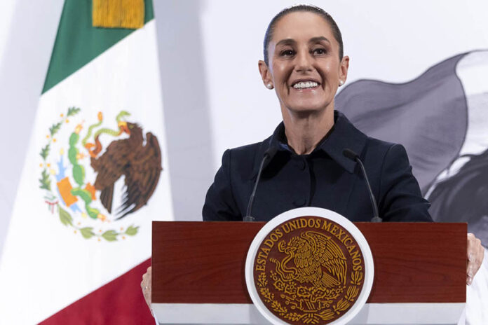 President Sheinbaum smiles from behind a podium next to a Mexican flag