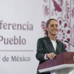 President Sheinbaum smiles from behind a podium next to a banner reading "Conferencia del Pueblo"