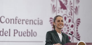 President Sheinbaum smiles from behind a podium next to a banner reading "Conferencia del Pueblo"