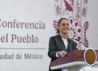 President Sheinbaum smiles from behind a podium next to a banner reading "Conferencia del Pueblo"