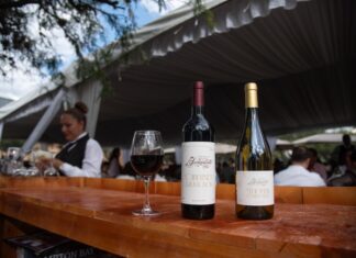 Wine bottles and a fresh pour of red wine sitting on a bar