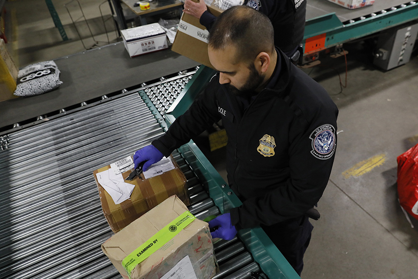 A US customs and border patrol officer inspects mail packages along a conveyor belt