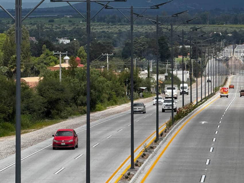 A multi-lane highway running through a small-town Mexico. The recently modernized road features fresh pavement, a landscaped median, and a long row of new, solar-powered streetlights. The road connects San Miguel de Allende and Dolores Hidalgo in Mexico.