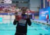 swimmer showing medal by a pool