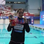 swimmer showing medal by a pool