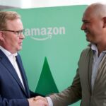 Two men shake hands in front of an Amazon logo in Mexico City