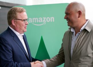 Two men shake hands in front of an Amazon logo in Mexico City