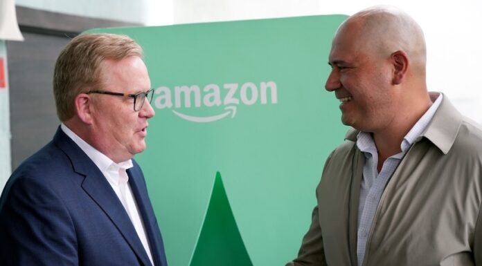 Two men shake hands in front of an Amazon logo in Mexico City