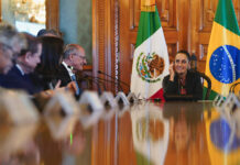 Sheinbaum and Brazil Vice President Geraldo Alckmin sit at a long table with bureaucrats in front of Mexican and Brazilian flags