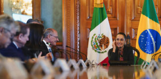 Sheinbaum and Brazil Vice President Geraldo Alckmin sit at a long table with bureaucrats in front of Mexican and Brazilian flags