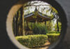 A circular framing shows a Japanese-style gazebo with a dark tiled roof and ornate trim, nestled among trees and manicured hedges in a park.