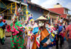 Costumed dancers in vibrant masks and traditional clothing parade through the streets during a Mexican festival in Xico, Veracruz, with colorful banners and colonial buildings in the background.