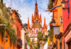 A vibrant photo of the pink neo-Gothic spires of the Parroquia de San Miguel Arcángel in San Miguel de Allende, Mexico, viewed from a city street.