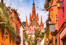 A vibrant photo of the pink neo-Gothic spires of the Parroquia de San Miguel Arcángel in San Miguel de Allende, Mexico, viewed from a city street.