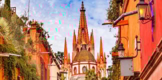 A vibrant photo of the pink neo-Gothic spires of the Parroquia de San Miguel Arcángel in San Miguel de Allende, Mexico, viewed from a city street.