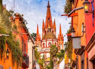 A vibrant photo of the pink neo-Gothic spires of the Parroquia de San Miguel Arcángel in San Miguel de Allende, Mexico, viewed from a city street.