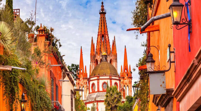 A vibrant photo of the pink neo-Gothic spires of the Parroquia de San Miguel Arcángel in San Miguel de Allende, Mexico, viewed from a city street.