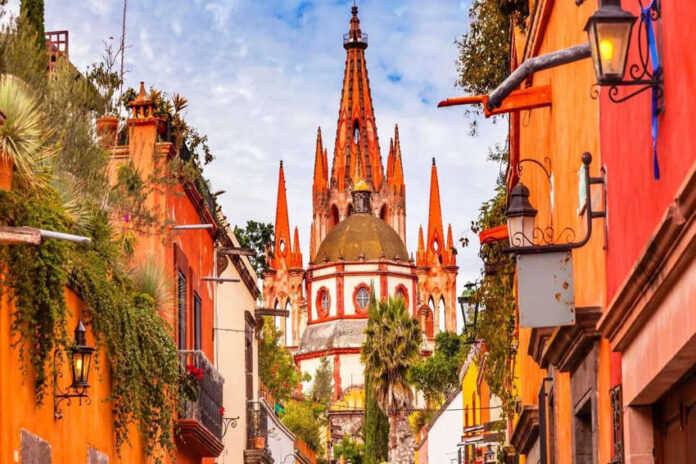 A vibrant photo of the pink neo-Gothic spires of the Parroquia de San Miguel Arcángel in San Miguel de Allende, Mexico, viewed from a city street.